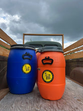 Load image into Gallery viewer, Two colorful barrels with a visible logo in the back of a old farm Truck against a cloudy sky.