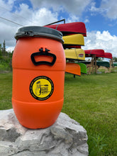 Load image into Gallery viewer, Orange food barrel with a yellow label on a rock, with canoes in the background.
