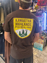 Load image into Gallery viewer, Person wearing a brown t-shirt with 'Kawartha Highlands Provincial Park' design.
