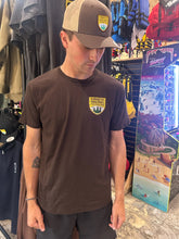 Load image into Gallery viewer, Man wearing a brown Kawartha Highlands Park t-shirt with a logo in a store setting
